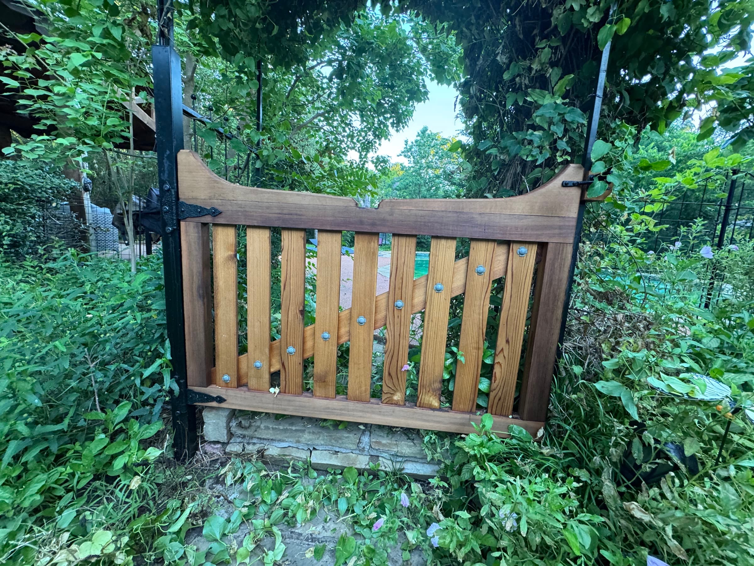 Scalloped-top garden gate with copper-headed slats.