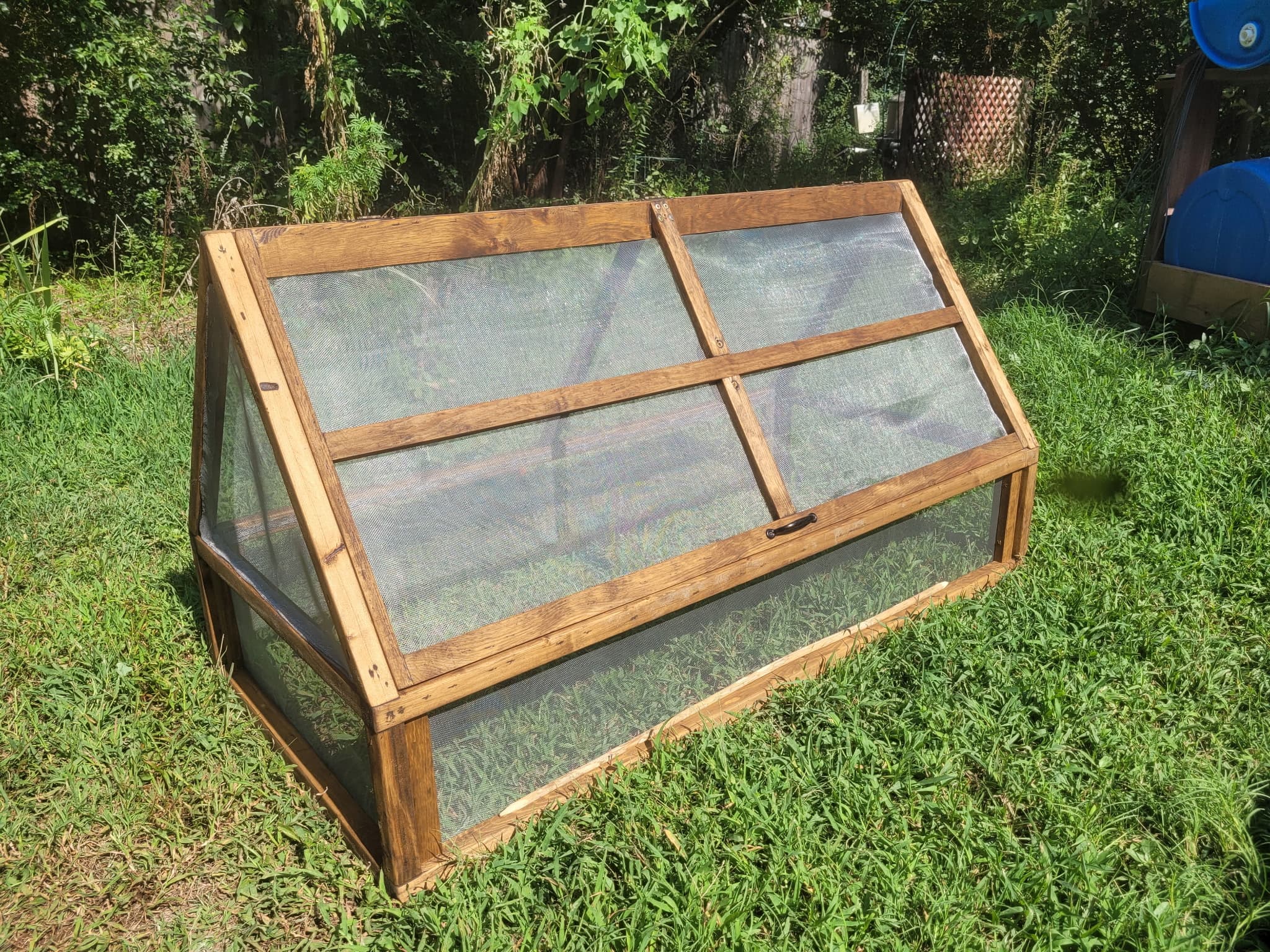 A pitched-roof cold frame with hinged screened panels.