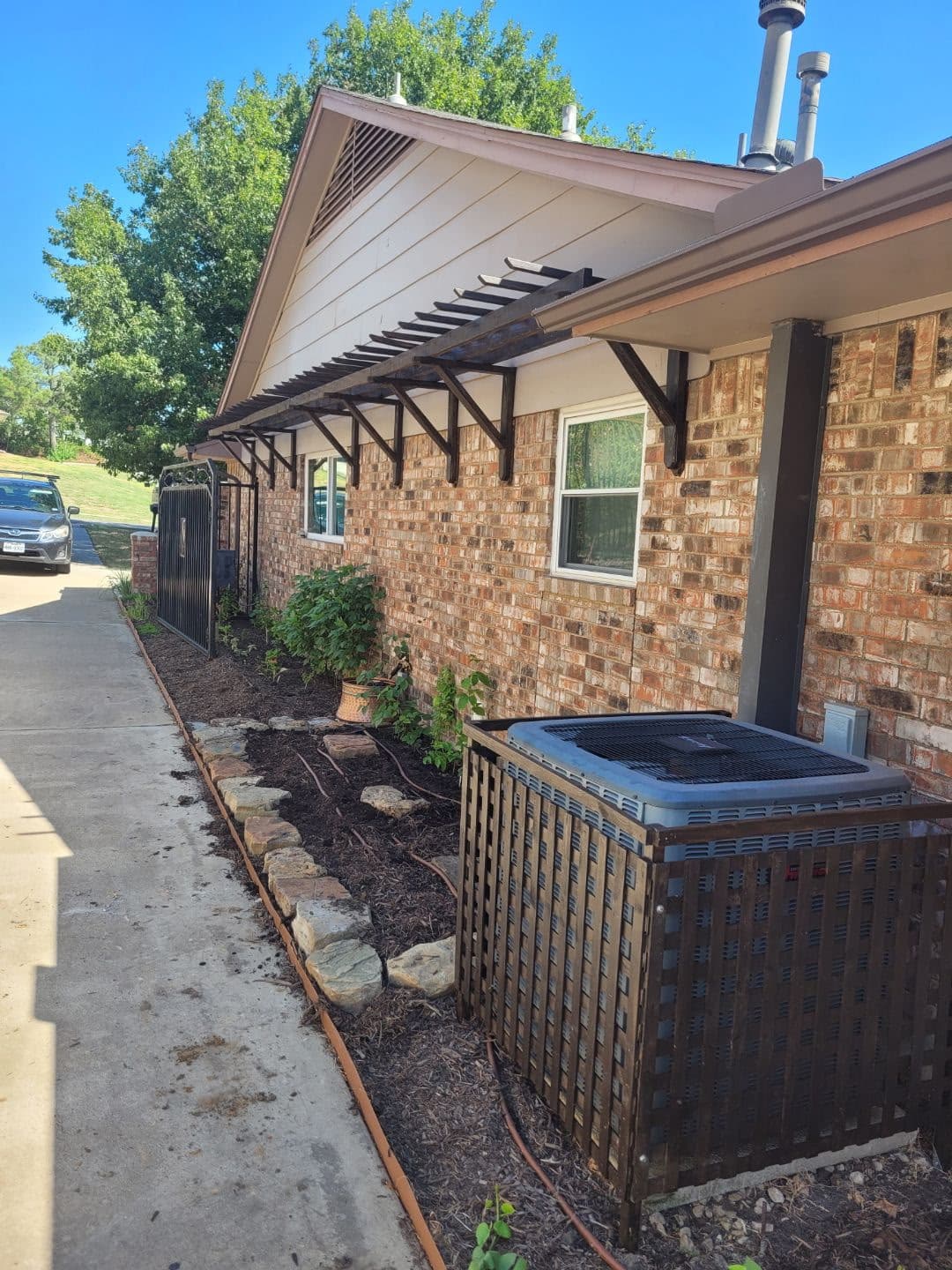 Stained-cedar pergola brackets along a brick exterior.